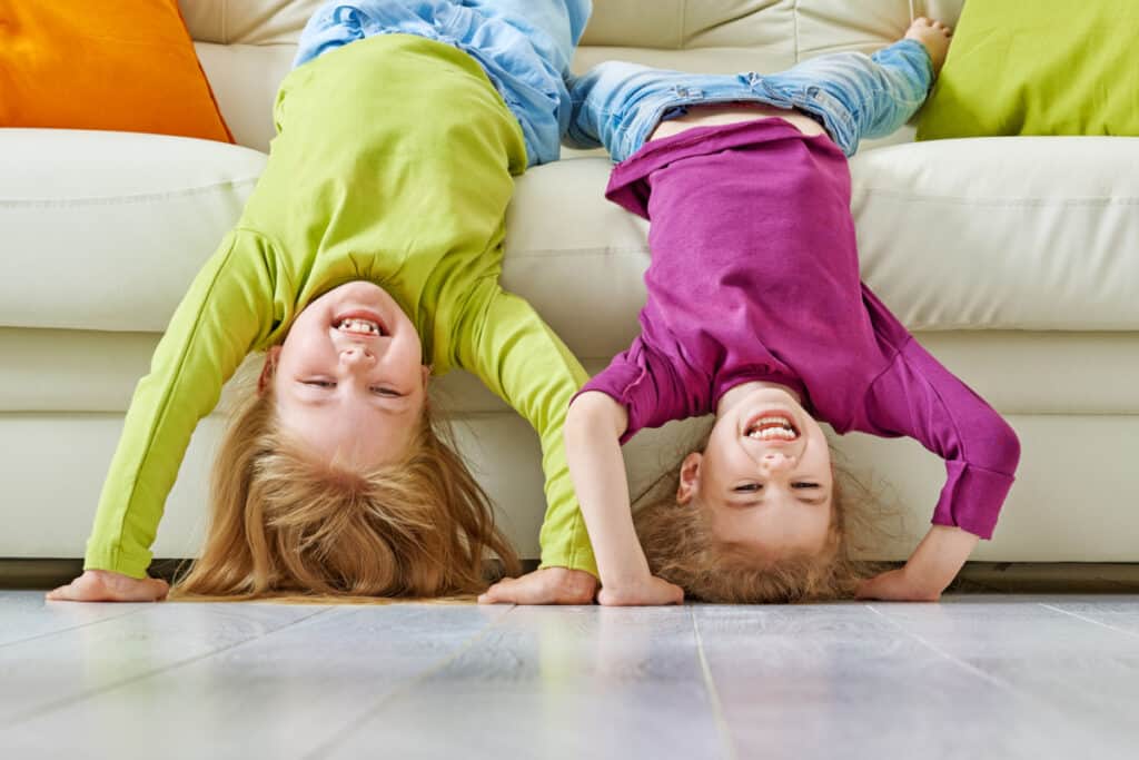 Two kids hanging upside down over a couch, laughing.