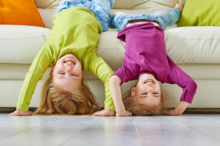 Two kids hanging upside down over a couch, laughing.