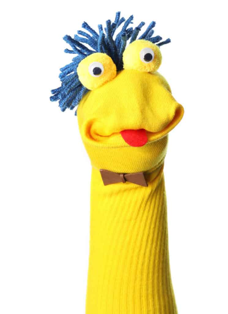 Yellow sock puppet with googly eyes, a red felt tongue, a brown bowtie and blue yarn hair.