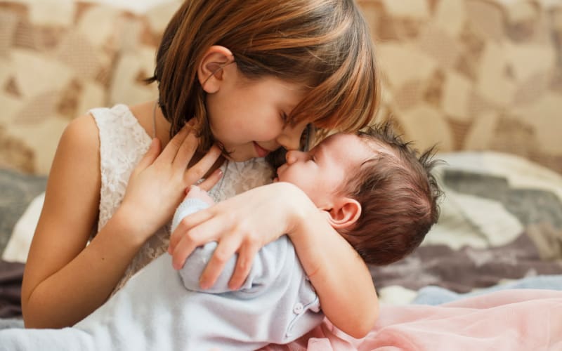 little girl with short dark hair cradling her baby brother in her arms