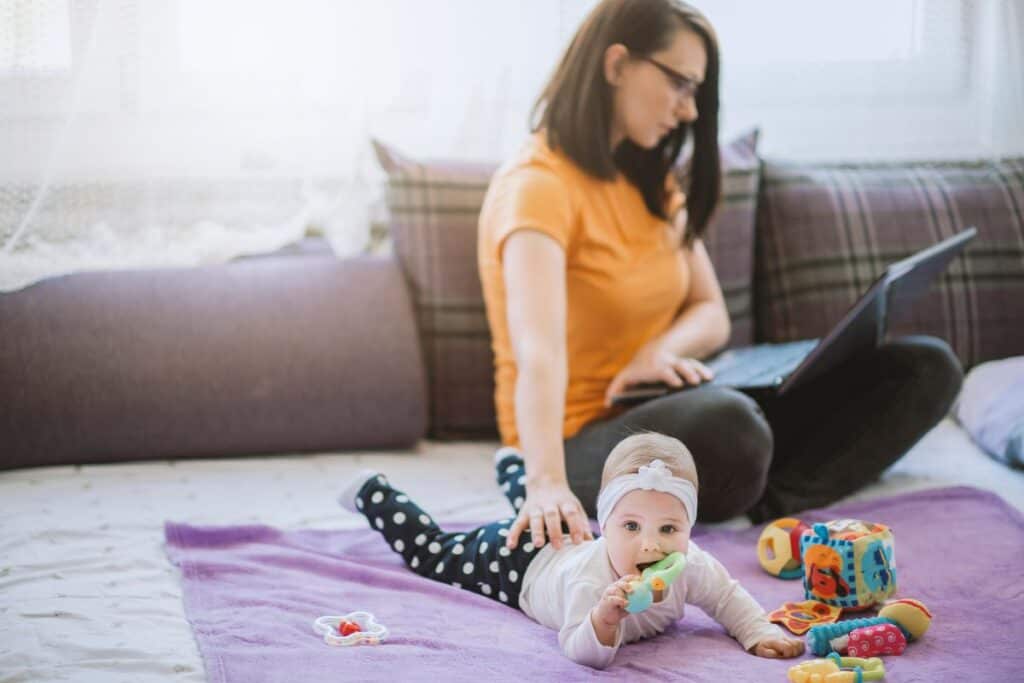 Woman working at home with baby playing on the floor.