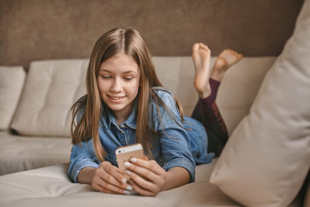 Tween girl on couch using iphone.