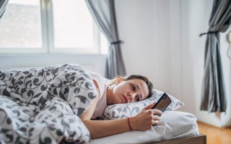 Woman scrolling social media in bed, frowning.
