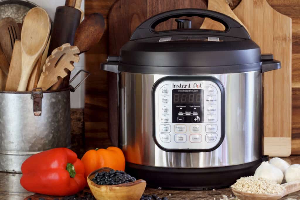 Instant pot in front of wooden cutting boards and utensils on a kitchen counter.
