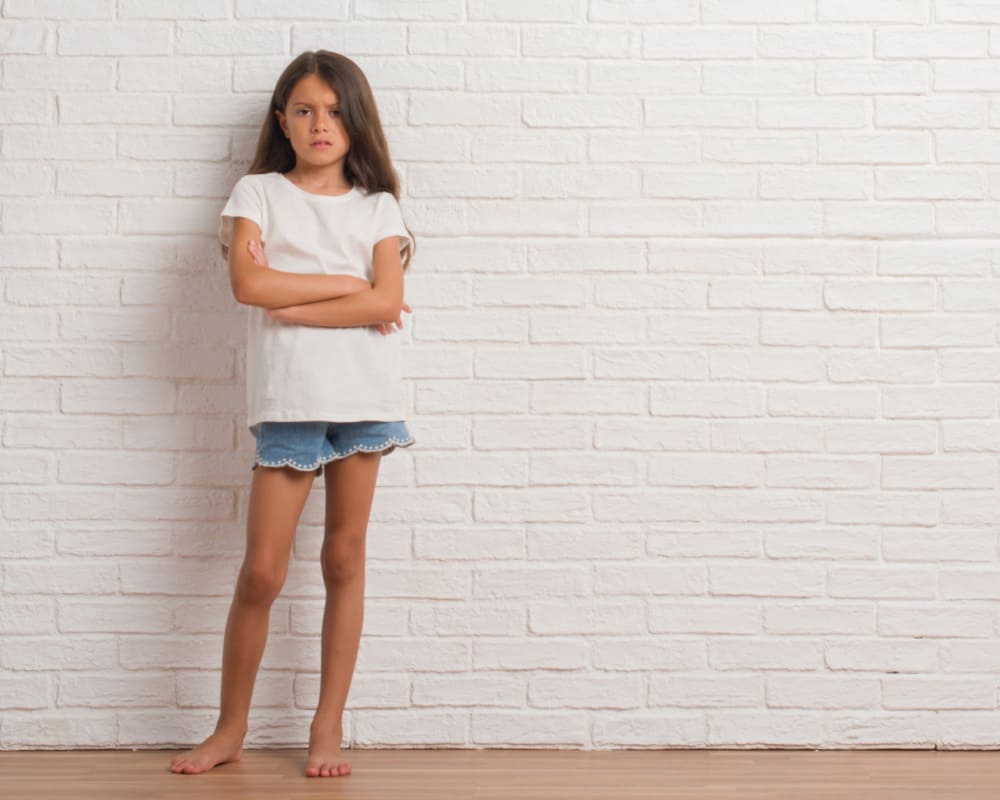 Young girl standing against a brick wall with arms crossed: portraying concept of sassy behavior and back talk