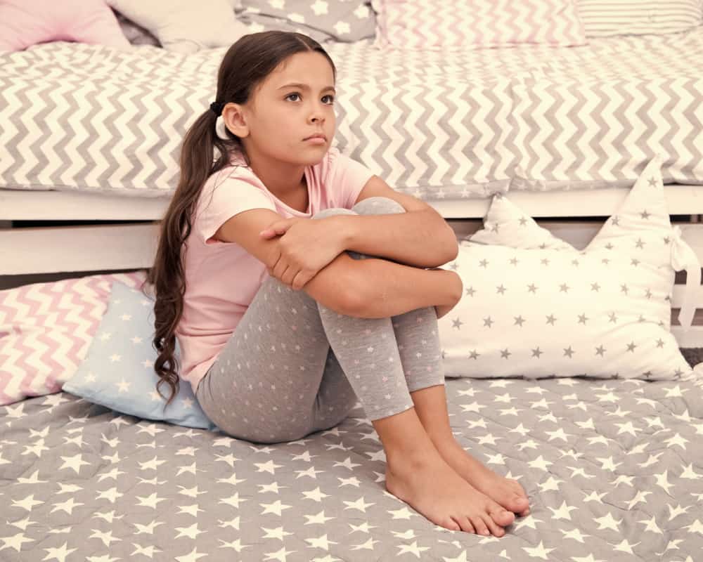 Image of a daughter sitting in her room with arms on her knees; concept of parenting a tween girl: giving her space