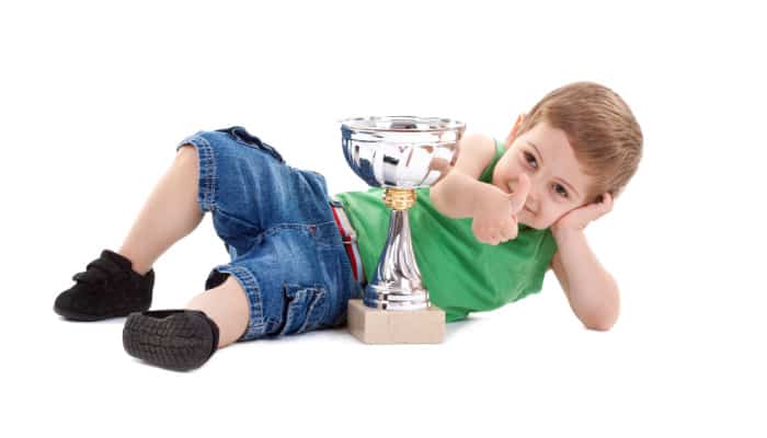 Little boy laying on the floor with a thumbs-up sign and a trophy: concept of potty training rewards- ineffective eventually