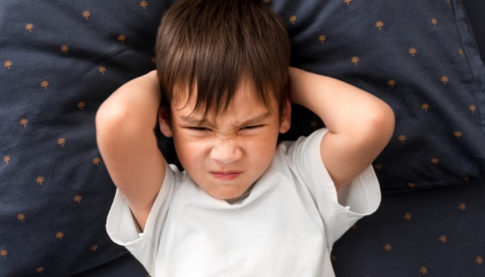 Toddler boy grimacing at the camera while laying in bed: example of stubborn toddler refuses to potty train