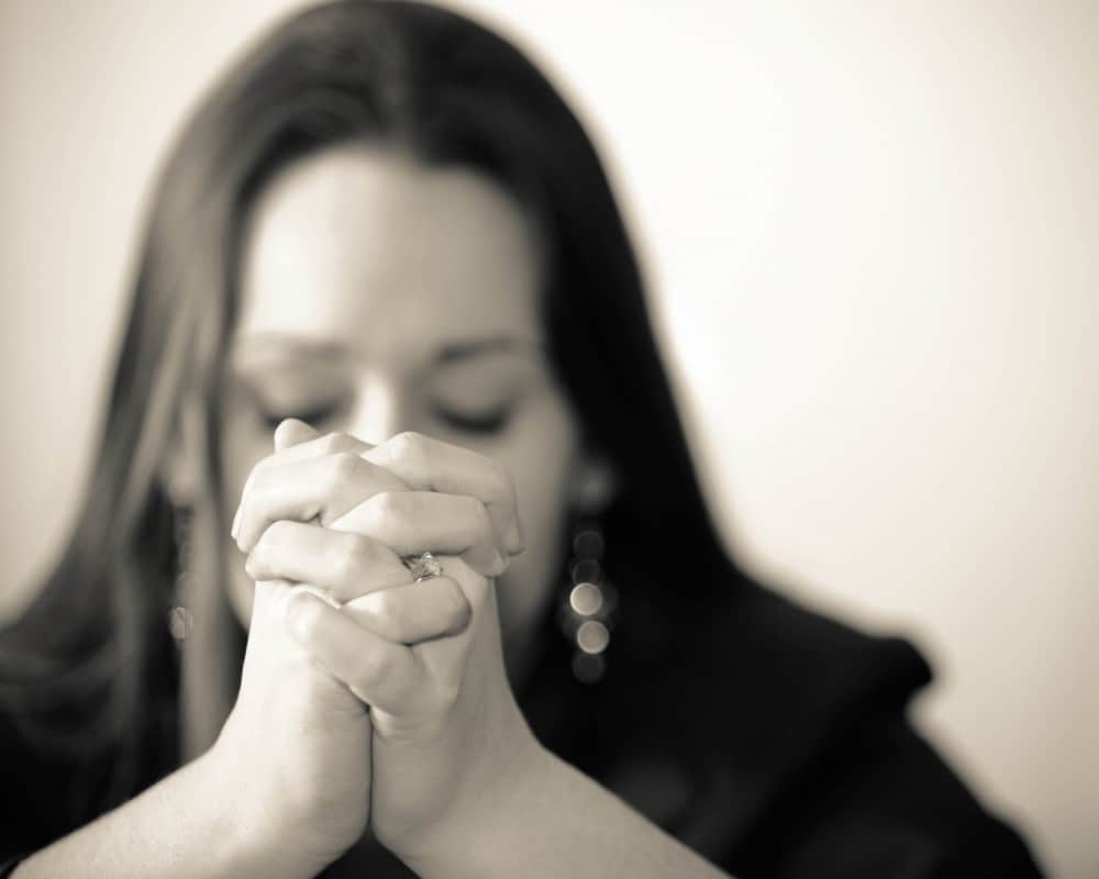 Image of mom in deep prayer with hands folded; concept of trusting God with our fears to cast out worry