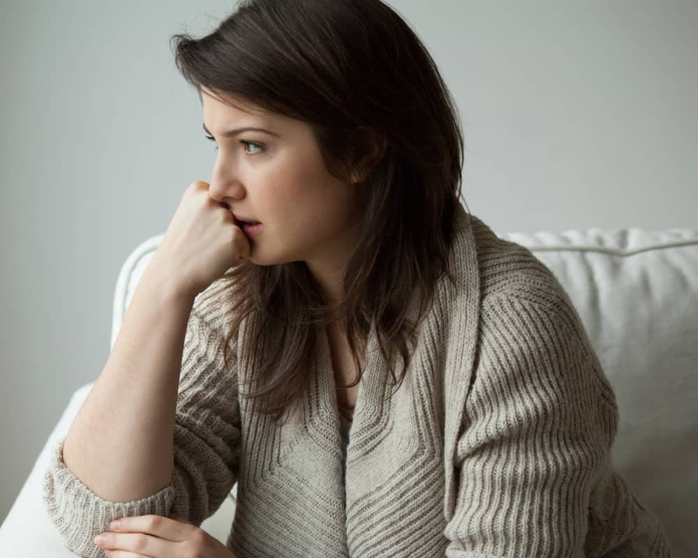 Image of a woman sitting on a couch looking worried; concept of Bible verses for worried moms