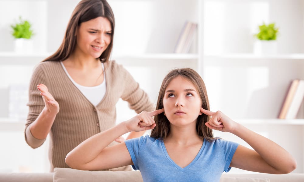 tips for moms of teen girls- mom with teen daughter who has fingers in her ears, ignoring her.