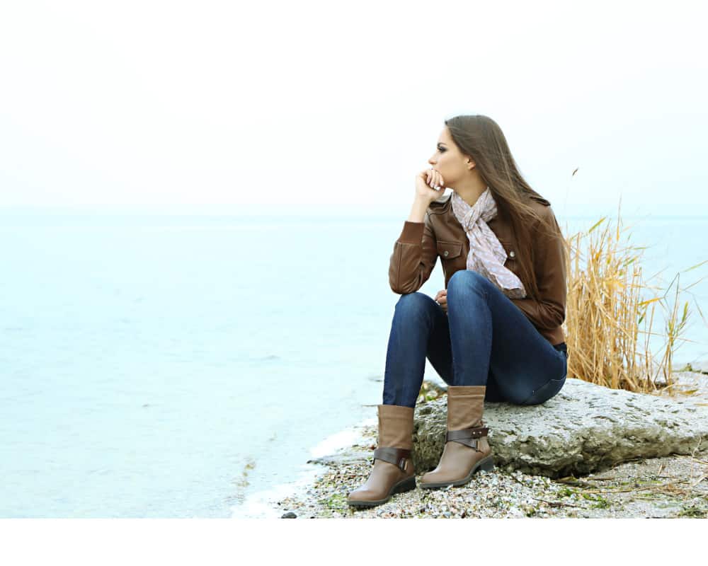 anxious mom thinking, sitting on a rock cliff- concept of giving your worry to God in prayer and praise.