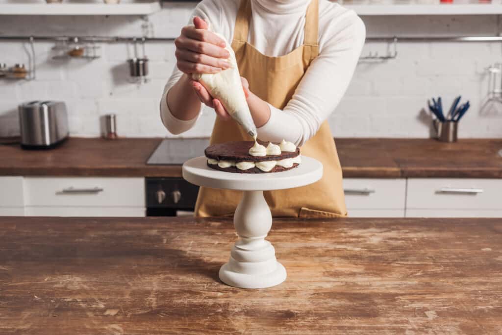 cake decorating hobby idea for moms: a woman adds icing to a cake on a white cake pedestal. 