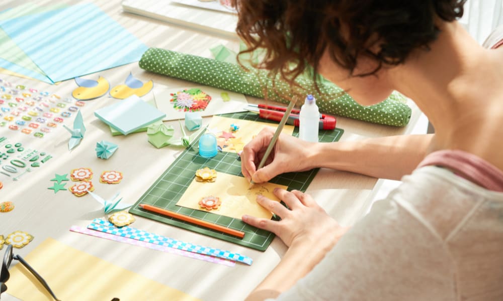 Crafting hobbies for moms at home: a woman working on a scrapbook page on a large craft table at home.