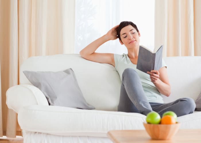 Woman sitting on a couch reading a novel; concept of -doing too much for your child? take time for yourself 