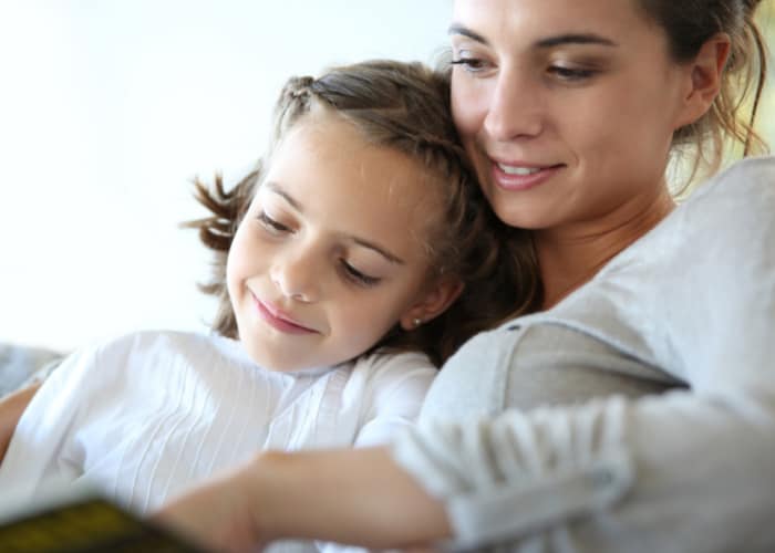 Smiling mom sitting on couch, reading to young daughter.