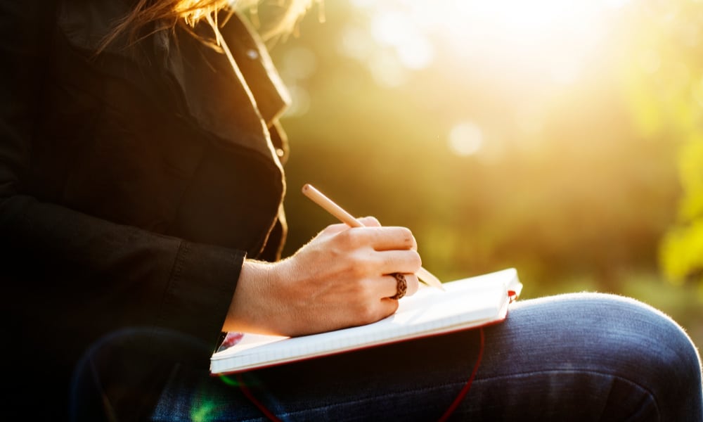 Writing as a hobby for moms: a woman writing in a notebook outdoors.