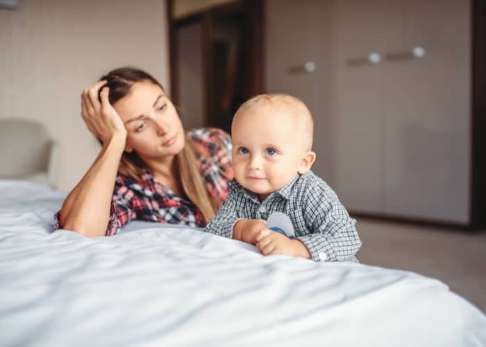 Image of a worried young mom watching her baby boy on the bed.