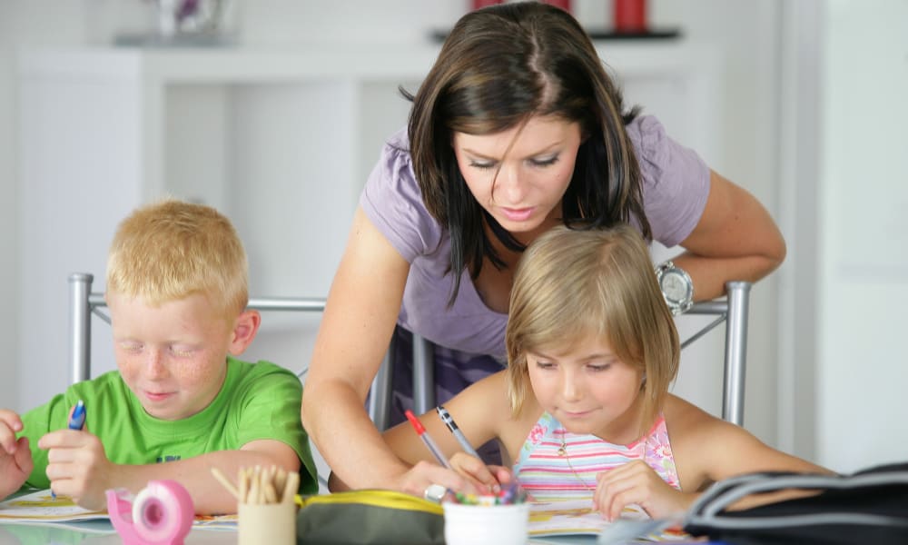 Concept of why moms need hobbies- demands of motherhood: mom helping her two children with homework.