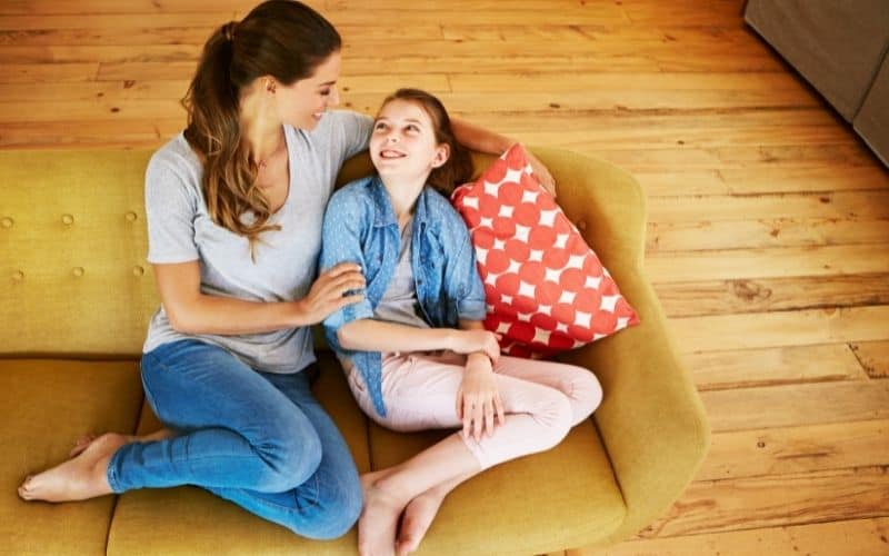 Mom smiling down at teen daughter on the couch- going out of our way to notice responsible behavior