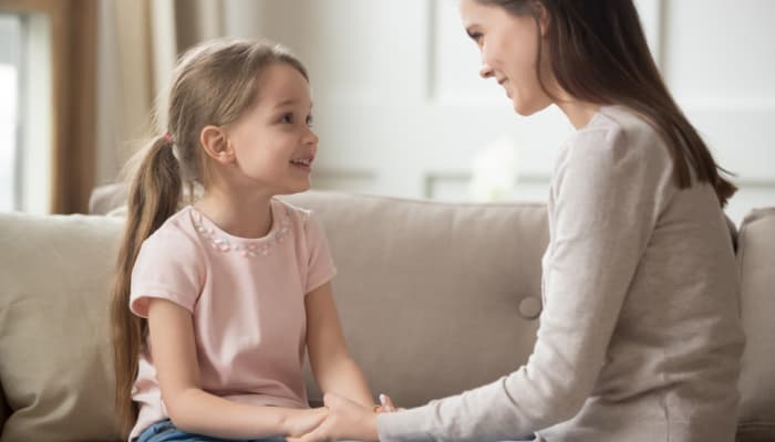 Teaching respect to children -how to practice it: example of mom talking to young daughter on the couch about respectful behavior.