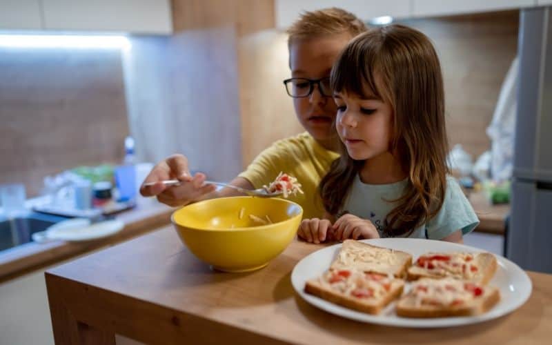 concept of how to raise a responsible child -two siblings fixing snacks in the kitchen.