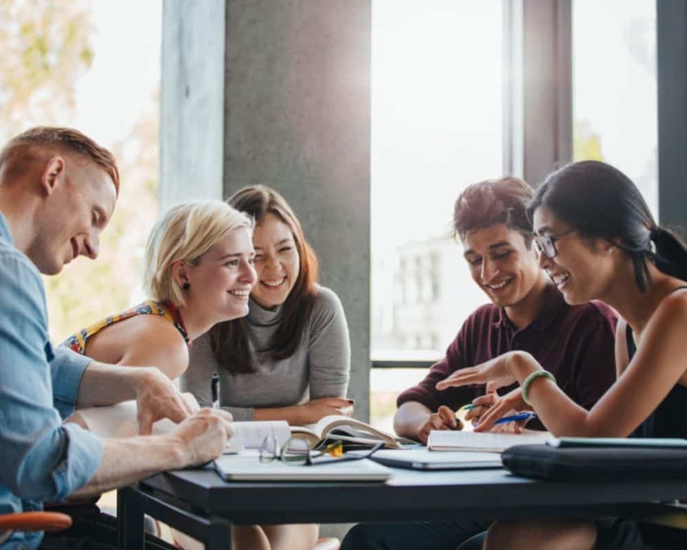 A group of smiling college students studying around a table. Prayer for college students.