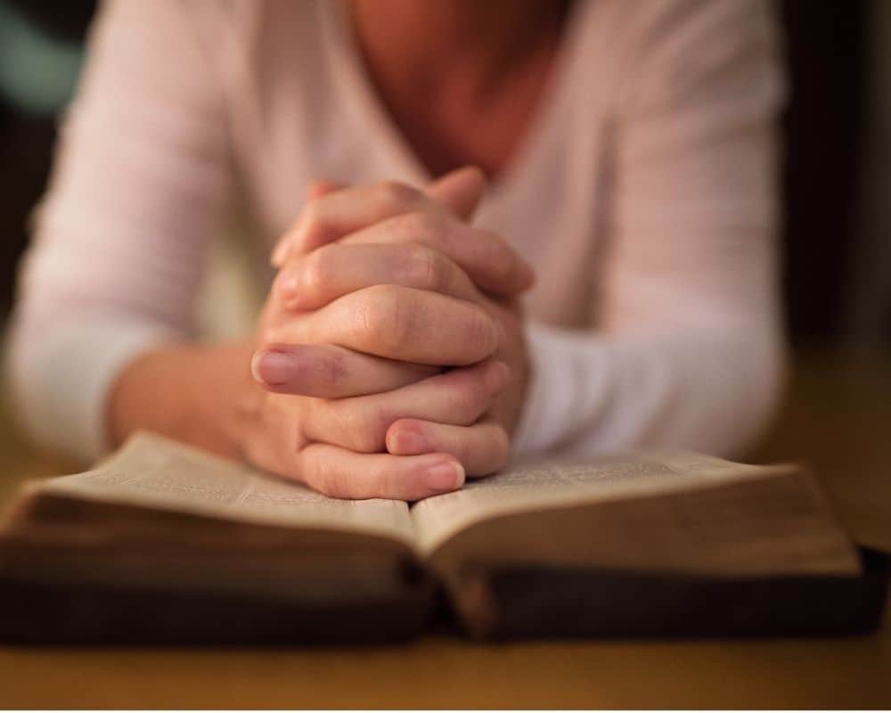 Woman with hands folded in prayer over her Bible- How to pray for your child at school