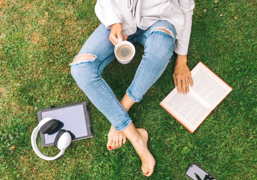 Woman sitting outside with headphones, ipad, book - concept of Bible study podcast for women