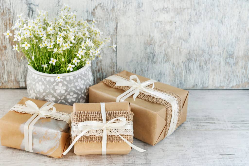 Gifts wrapped in brown craft paper and ribbon with fresh flowers nearby on a whitewashed table.