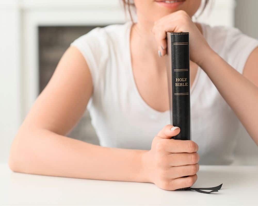 Image of woman resting her chin on the spine of a Bible. Christian parenting concept.