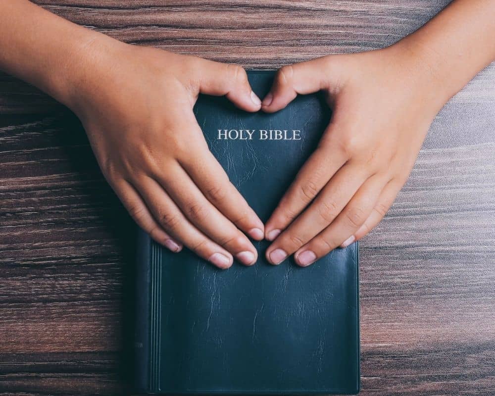 Image of Bible with hands shaped into a heart around the Title.