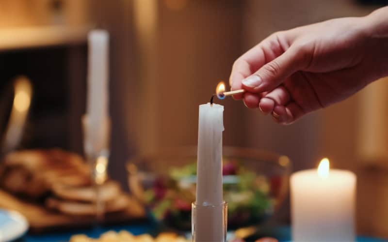 Image of woman lighting candles for a family Christmas eve dinner with a salad and bread in the background.