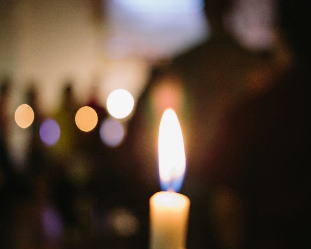 Image of candle burning with Christmas lights in background- candlelight church service concept.