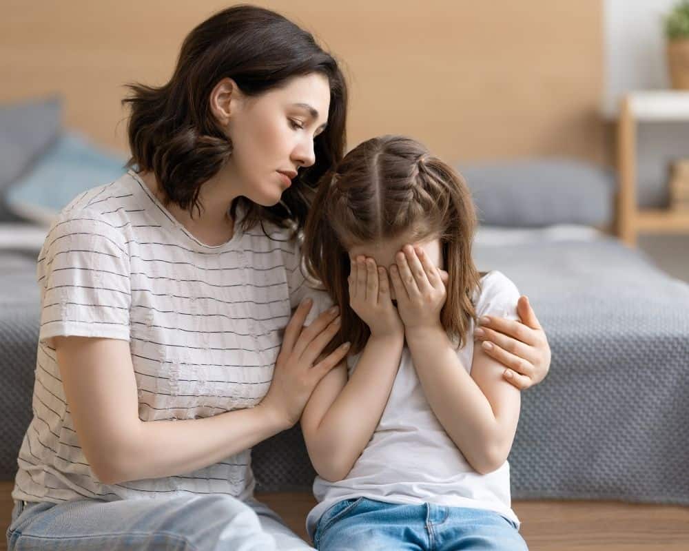 Mom consoling upset child, leaning against the bed. Concept of forgiveness.