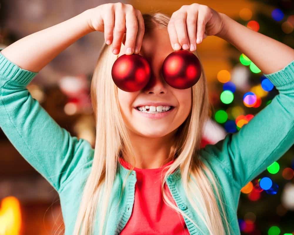 Image of girl  holding Christmas ornaments up, grinning.