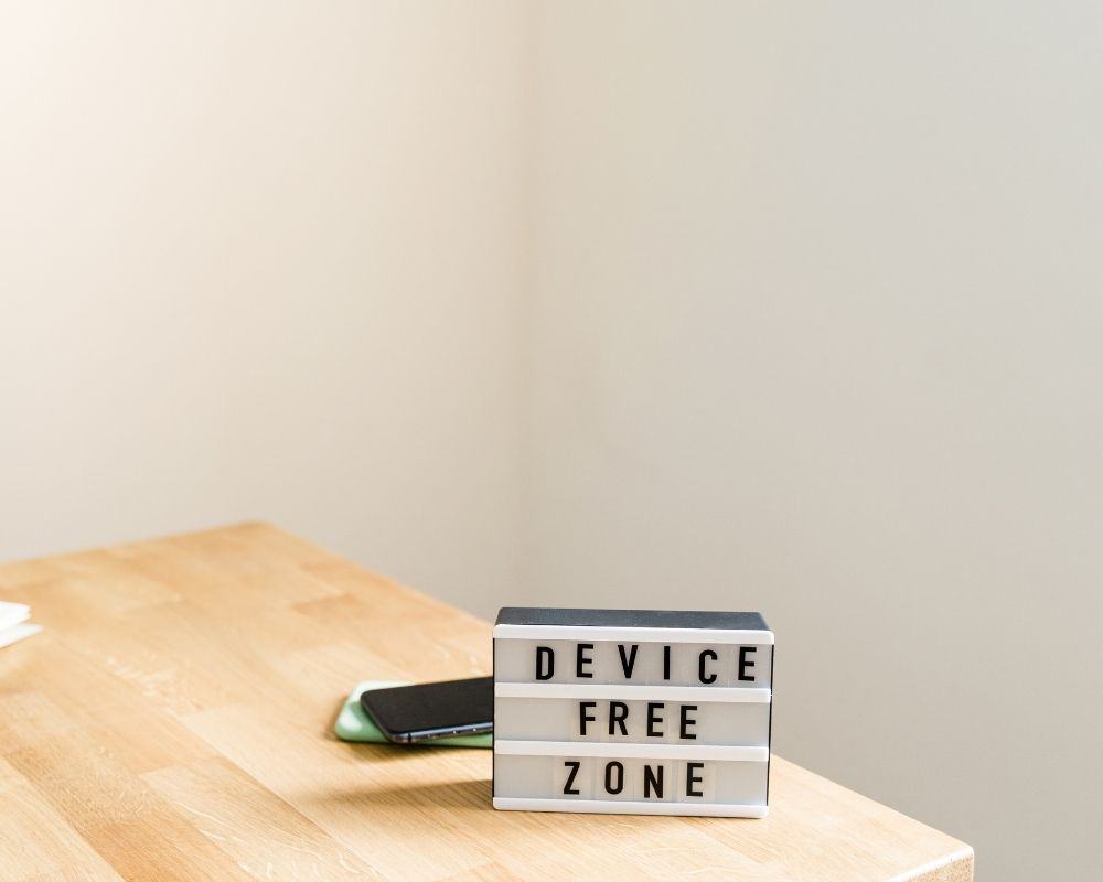 Image of letterboard sign on kitchen table that reads "device free zone" with cell phones stored behind it.