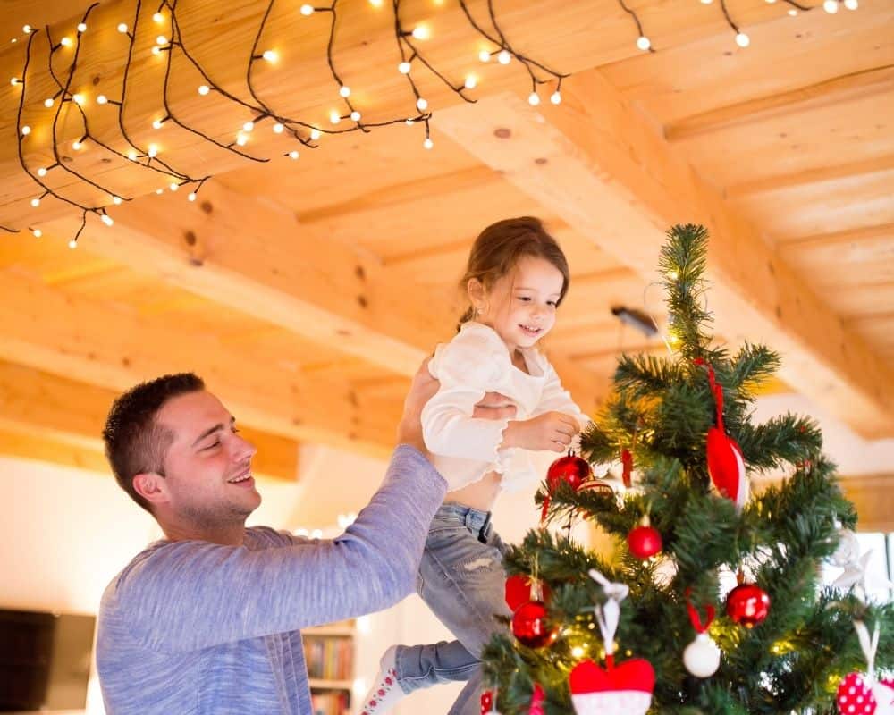 Image of Dad and daughter decorating Christmas tree- concept of meaningful Christmas traditions.