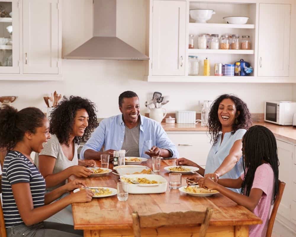 Image of African American family enjoying a dinner together- mother, father, preteen daughter and two teen daughters, smiling and laughing together.