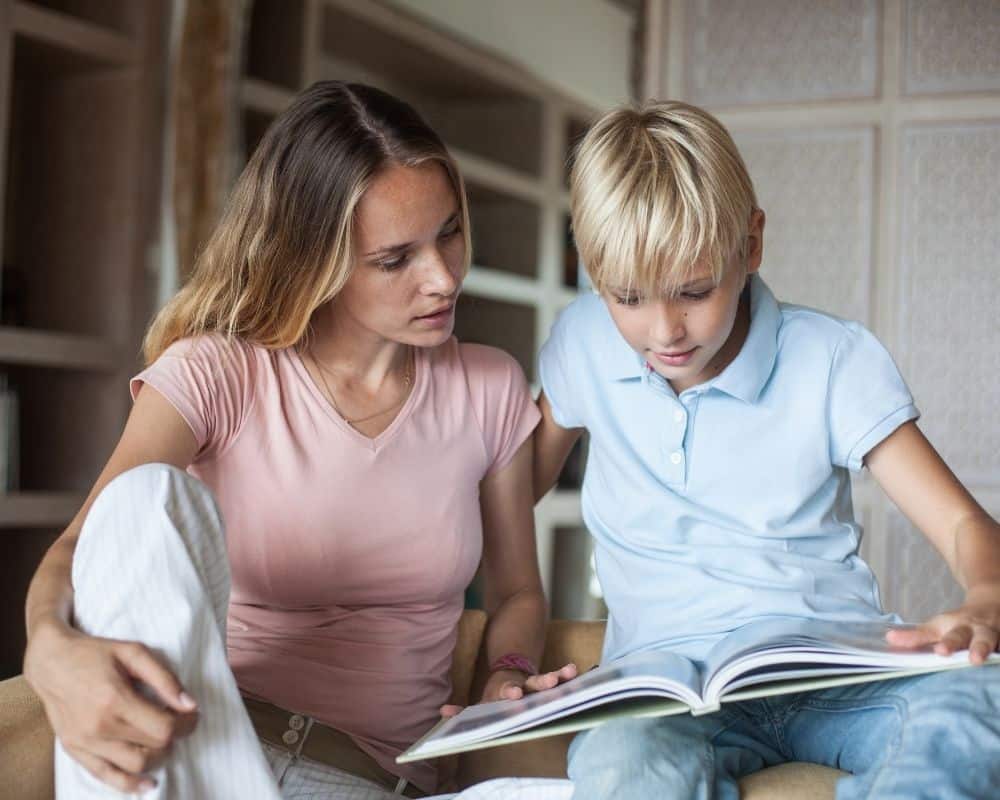 Image of young mom sitting with 10-year-old son, reading a non-fiction book together with interest.