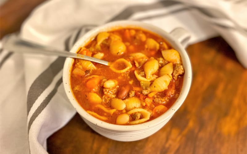 Image of finished pasta e fagioli in a small white bowl on a wooden table.