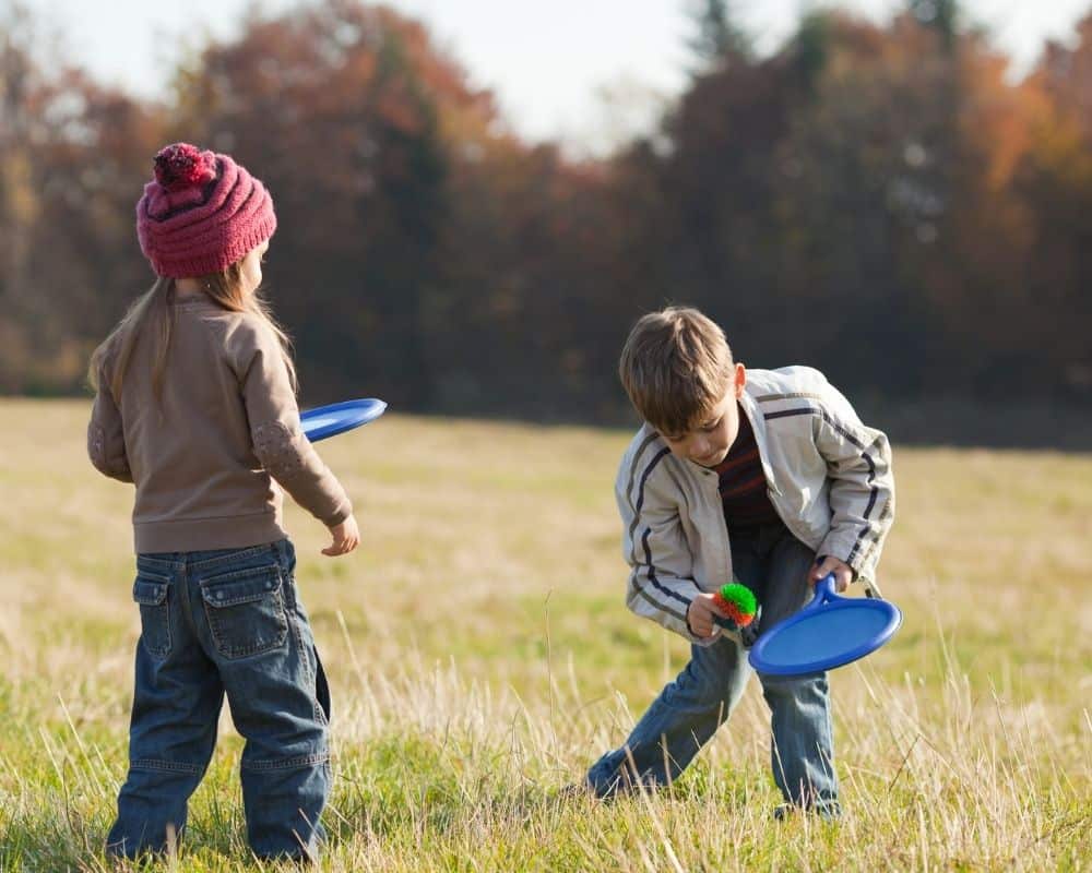 Two kids playing outside together with a ball and catching mitt. Concept of creative play.