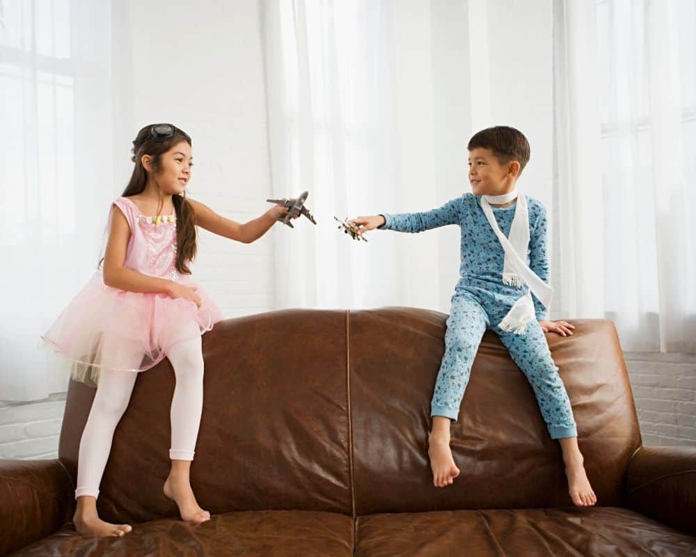 Image of boy and girl siblings playing pretend with airplanes and props on a couch.