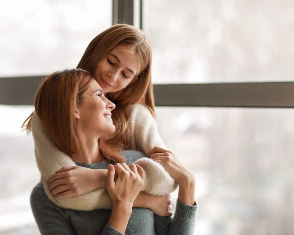 Image of young daughter with arms around her mother, smiling.