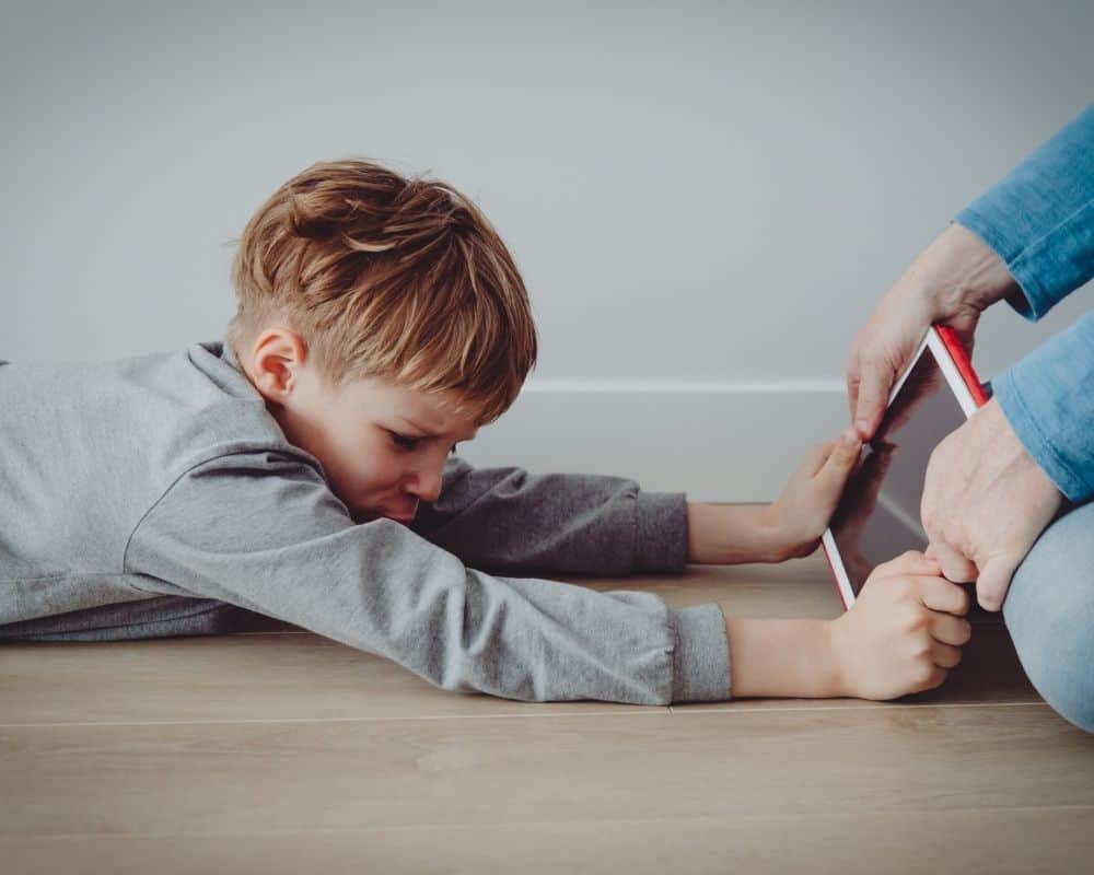 Image of angry grade school boy holding onto electronic device -tablet- while mom tries to take it away.