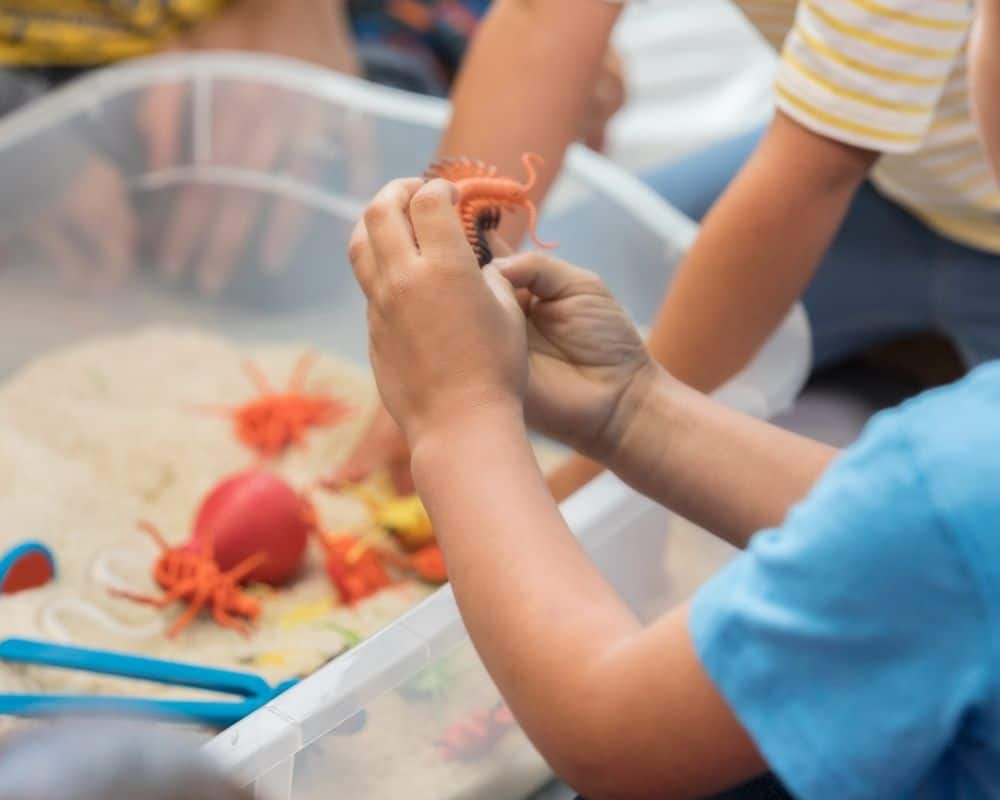 Image of child digging up plastic insects in a sensory bin made at home.