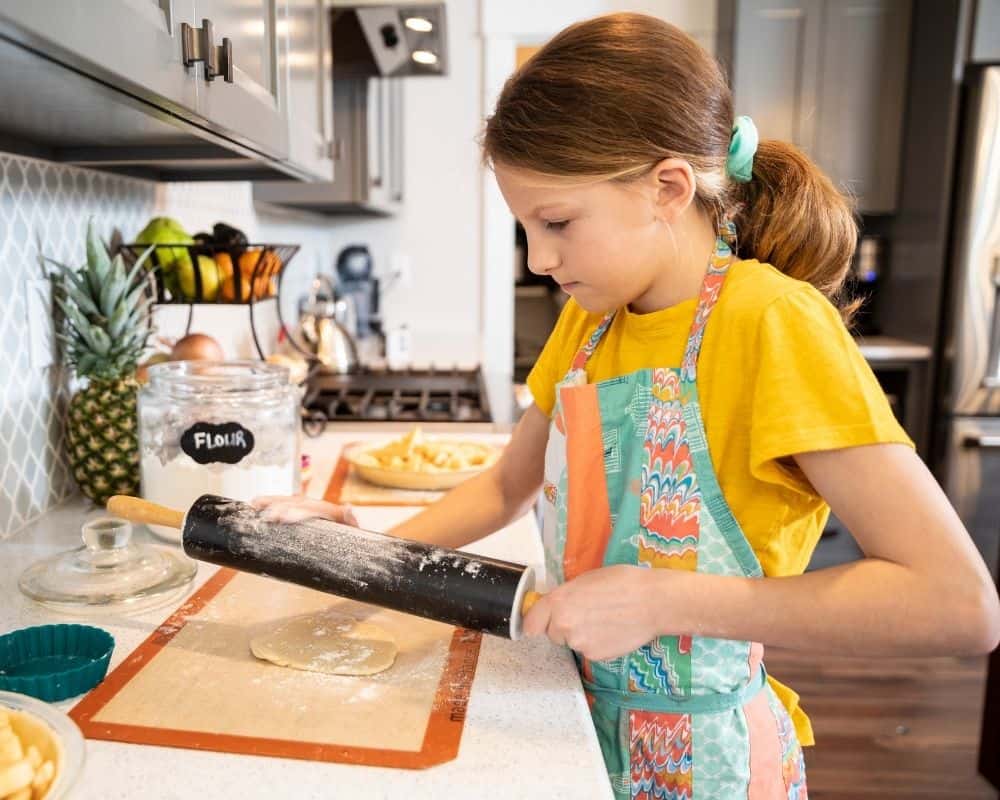 Image of preteen girl rolling out dough on a kitchen counter. Concept of teaching kids to bake as a fun indoor activity.
