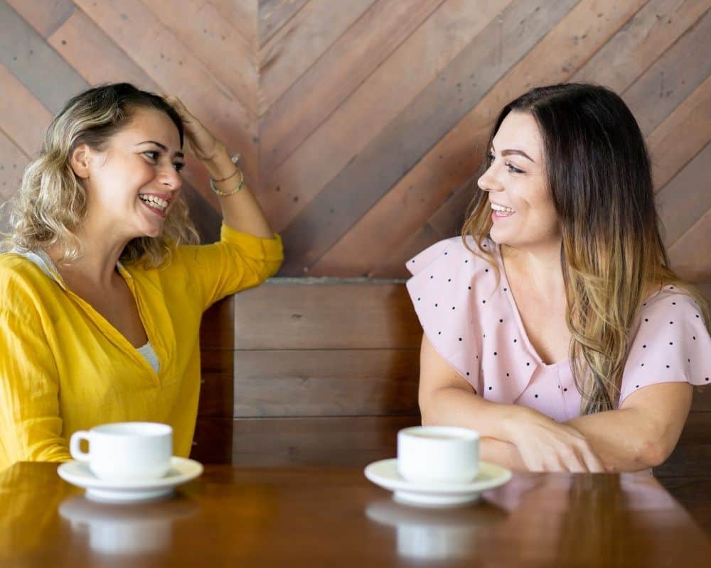Image of two women at a coffee shop, smiling and sharing stories. Concept of Christian women mentoring other Christian women.