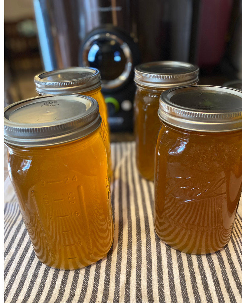 Four quart jars of home-canned chicken stock cooling off on a kitchen towel on the counter.