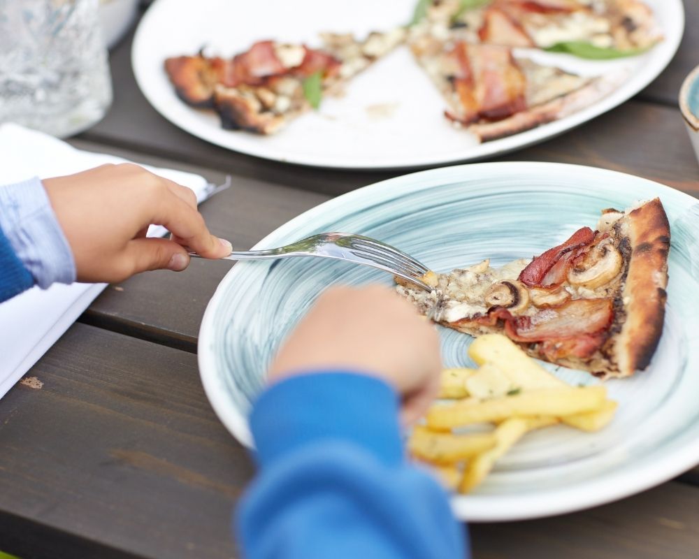 Child eating a slice of pizza and fries.